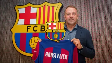 Hansi Flick holds the FC Barcelona jersey with his name on it and the FC Barcelona badge is in the middle.